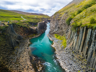 A scenic view of Studlagil Canyon in Iceland with basalt columns and a turquoise river.