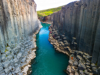 A scenic view of Studlagil Canyon in Iceland with basalt columns and a turquoise river.
