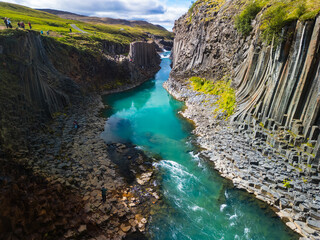 A scenic view of Studlagil Canyon in Iceland with basalt columns and a turquoise river.