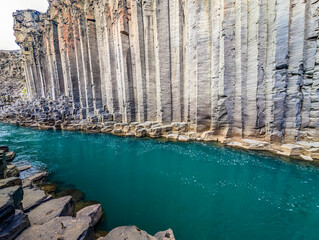 A scenic view of Studlagil Canyon in Iceland with basalt columns and a turquoise river.