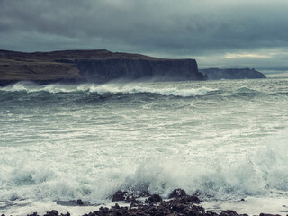 The ocean is rough and the sky is cloudy. The waves are crashing against the rocks. Scene is tense and dramatic. Nobody, Dark and moody nature background.