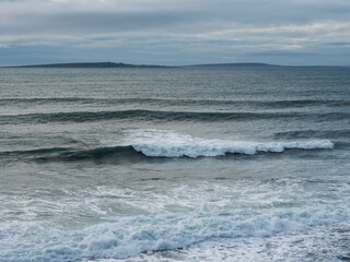 Rough stone coast, ocean waves and Aran islands in the background. Cloudy sky, Burren area, Ireland. Irish nature scenery. Nobody.