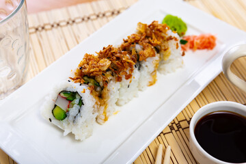 Plate is filled with crunch California rolls with fried puffed rice. Traditional Japanese food made from boiled rice, salmon, avocado and tender cheese. Dish is served with chopsticks, soy sauce.