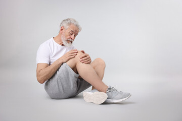 Senior man suffering from pain in his knee on light background. Space for text