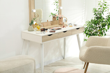 Makeup room. Dressing table with mirror, different beauty products, jewelry, armchair and houseplant indoors
