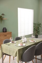 Stylish table setting with olive tablecloth, glasses and candles in dining room