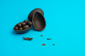 A whole and a broken chocolate Easter egg with small chocolate candies inside, placed on a vibrant blue background. A festive food photography concept ideal for holiday treats and celebrations.