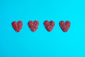 Four chocolate sprinkle hearts aligned on a blue background. A sweet and romantic composition, perfect for Valentine’s Day, greeting cards, love-themed designs, and dessert photography.