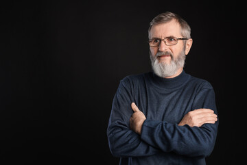 Fototapeta premium Portrait of mature man with crossed arms on black background, space for text