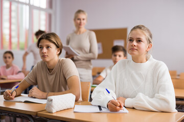 Portrait of teenage school girl and boy sitting together in classroom during lesson in secondary school