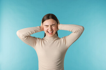 Frustrated woman covering her ears from loud noise on blue background