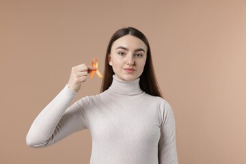 Multiple Sclerosis awareness. Young woman holding orange ribbon on beige background