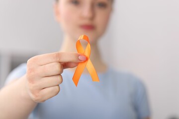 Multiple Sclerosis awareness. Young woman holding orange ribbon indoors, selective focus