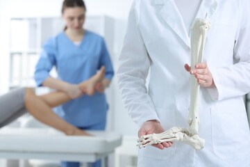 Doctor examining patient's foot in hospital, focus on medical worker with human leg skeleton
