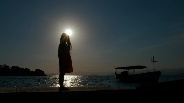 Hopeful child on pier in evening. A calm little girl admire the empty fishing boat on waves during sunset summer time.
