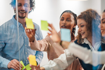 Businesspeople planning strategy using adhesive notes on glass wall in office