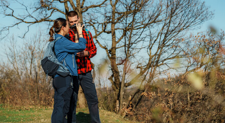 Young couple of hikers are resting and drinking water in the woods during beautiful sunny day, enjoying the fresh air and natural environment
