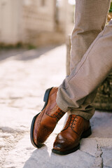 Man in brown shoes stands cross-legged on the paving stones. Cropped. Faceless