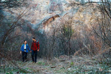 Obraz premium Young couple holding hands while hiking along a scenic trail near a rocky cliff in a bare forest, embracing the cool air of a tranquil autumn day filled with adventure