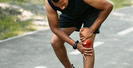 African American jogger suffering from pain in his knee during morning run at park