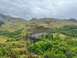 The iconic Glenfinnan Viaduct among the green hills of Scottish Highlands on a cloudy spring day. A breathtaking view of one of Scotland’s most famous railway bridges.