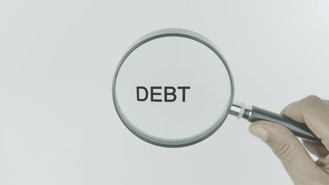 Debt text or word highlighted by a magnifying glass in a hand on a white background, symbolizing financial obligations, liabilities, and financial management