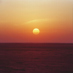 Sunset over a vast, dark plain. The sun is a brilliant yellow-orange.