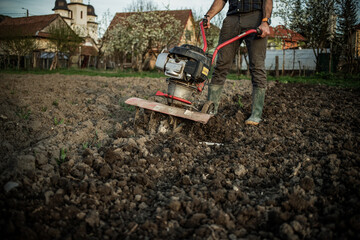 organic farming man ploughs the ground at sunset with a tiller preparing the soil for sowing