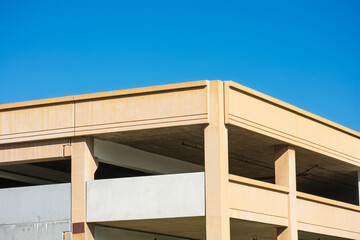 Corner view of a multi-level parking structure with beige concrete columns and railings, featuring open levels and exposed beams under a vibrant blue sky.