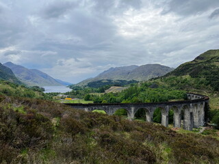 Naklejka premium The iconic Glenfinnan Viaduct among the green hills of Scottish Highlands on a cloudy spring day. A breathtaking view of one of Scotland’s most famous railway bridges.