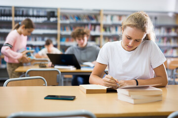 Portrait of teenager girl reading books and writing in notebooks in the library