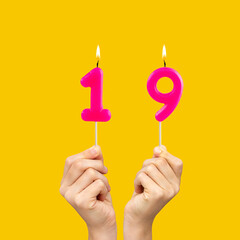 Hands holding birthday candles with number 19 - Yellow background