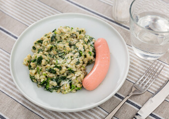 Appetizing meat sausages with pearl barley and spinach served on platter