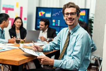 Portrait of businessman or analyst looking at camera with his colleague analyzing data analysis in dynamic business strategy investment planning meeting. Meticulous