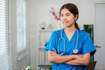 A healthcare professional in blue scrubs stands confidently with arms crossed in a modern medical...