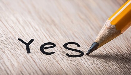 Pencil writing yes on a wooden surface with natural light highlighting the texture