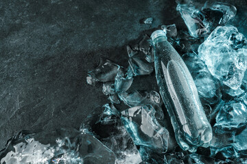 Bottle of water in ice on stone background. Pieces ice illuminated with blue light. Advertising...