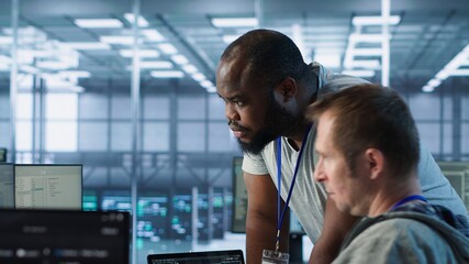 Programmer requesting help from manager while working on computer in data center, monitoring...