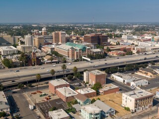 Obraz na płótnie Canvas Aerial view of Stockton, California, USA, showcasing the city's architecture, including office buildings, a church, and a shopping mall, alongside a busy highway with cars.