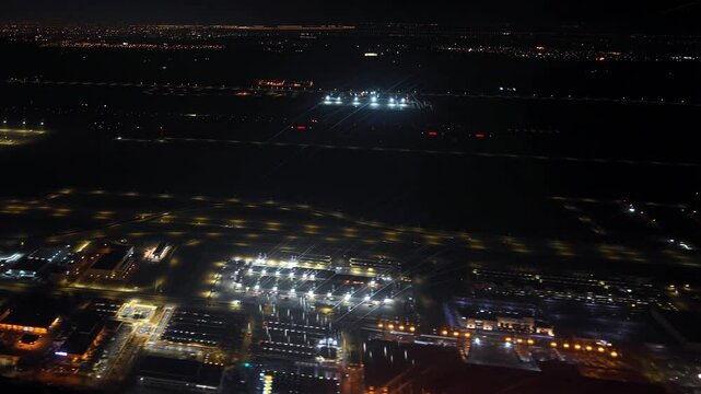 Airplane taking off from King Khalid International Airport at night, showing the brightly lit airport grounds and the city Riyadh in Saudi Arabia, lights in the distance. Aerial view