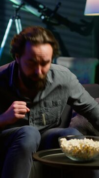 Vertical video Man in apartment chocking on food while watching movie on TV and eating popcorn. Person getting throat clogged while swallowing snack, doing heimlich maneuver on couch, fighting for his