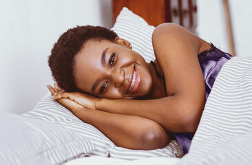 Morning with smile. Attractive african american young woman lies in bed in bedroom interior