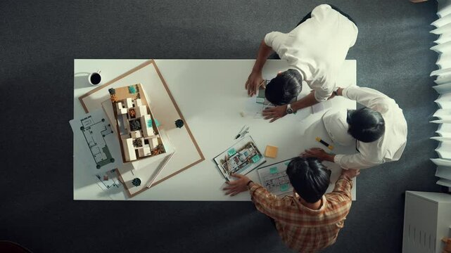 Group of skilled designer looking at model while discussing about building. Top view of architect engineer explain idea while talking and writing blue print scattering at meeting table. Alimentation.