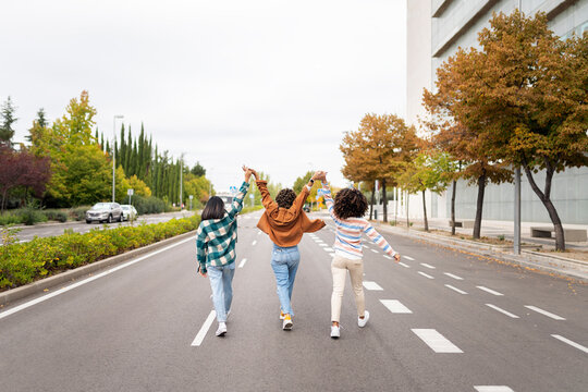 Three young women walking down a city street holding hands