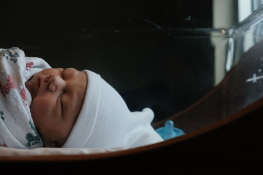 Newborn baby asleep in infant bed at hospital.