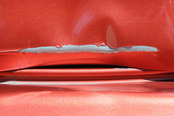 Close up of a red car with multiple visible scratches and paint damage The scratches expose the underlying metal, creating a contrast against the glossy surface. Perfect for automotive damage concepts