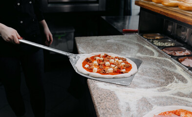 A chef placing a topped pizza on a baking peel in a pizzeria kitchen, showcasing fresh ingredients and culinary skills.