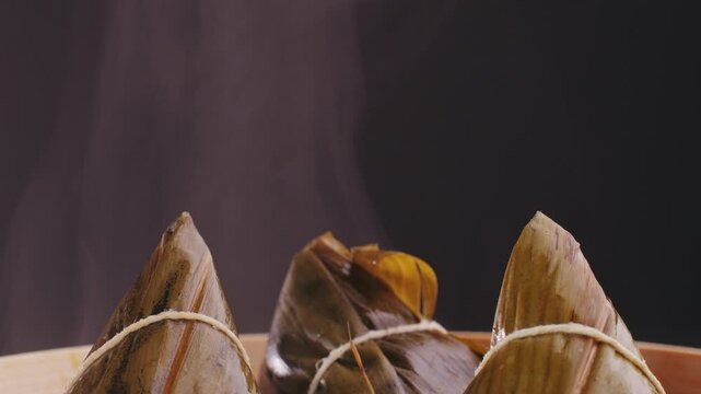 Hand holding zongzi (rice dumpling) with savoury fillings wrapped in bamboo or reed leaves.