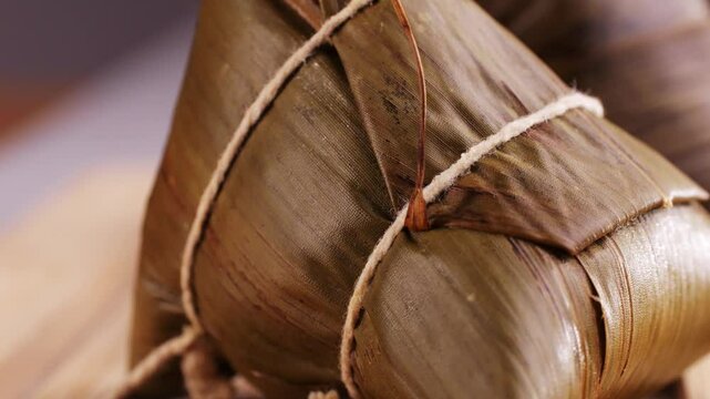 Hand holding zongzi (rice dumpling) with savoury fillings wrapped in bamboo or reed leaves.