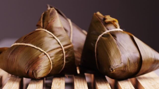Hand holding zongzi (rice dumpling) with savoury fillings wrapped in bamboo or reed leaves.